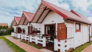 A row of white cottages with red roofs and wooden balconies, each with a small table and chairs. - Single-story Holiday Homes Close to the Beach (Ustronie Morskie)