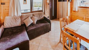 A cozy cabin interior with a sofa, a dining table, and a view of the outside. - Single-story Holiday Homes Close to the Beach (Ustronie Morskie)