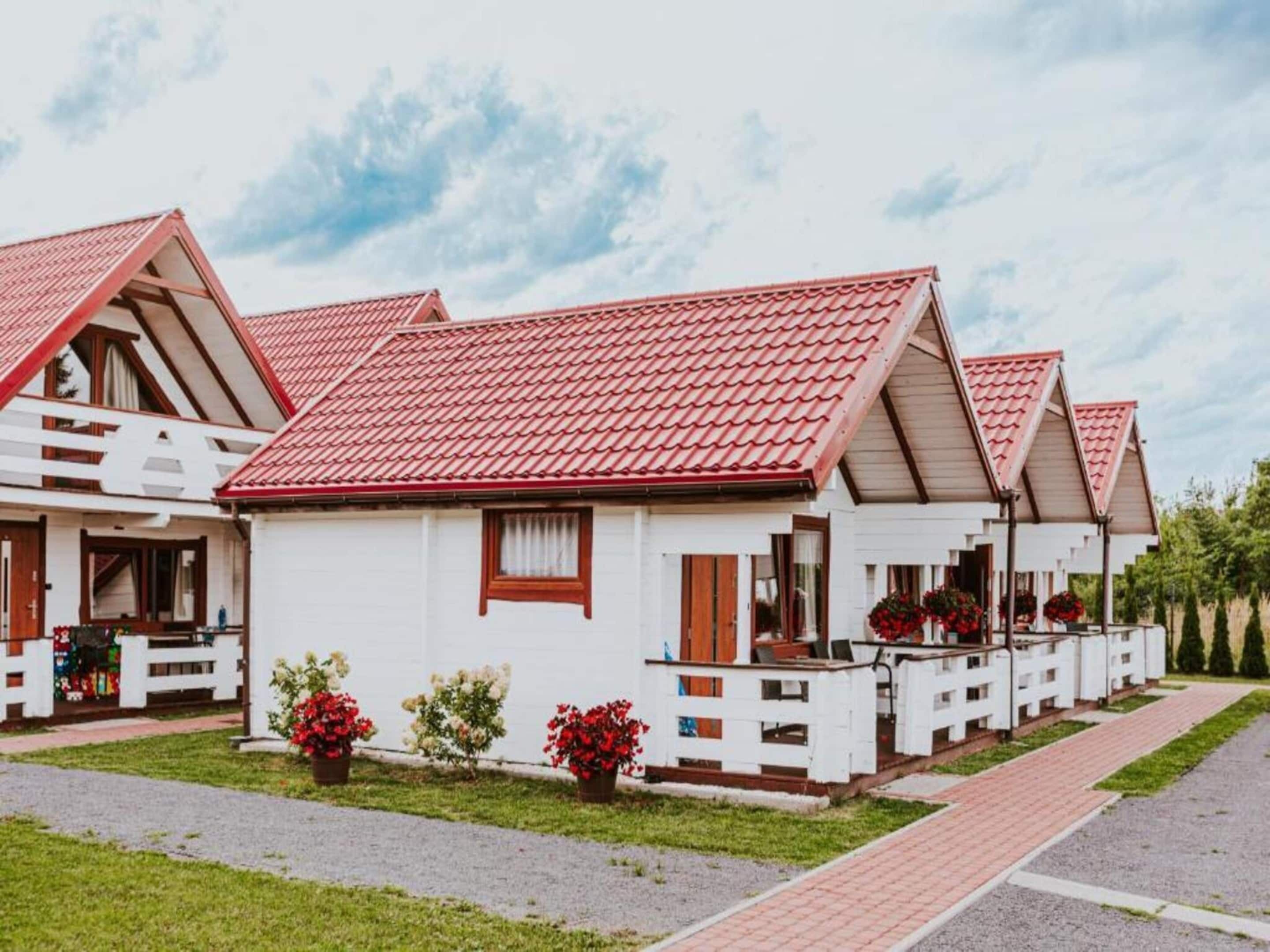 Uma fileira de cabanas brancas com telhados vermelhos e varandas de madeira, cada uma com um pequeno jardim.