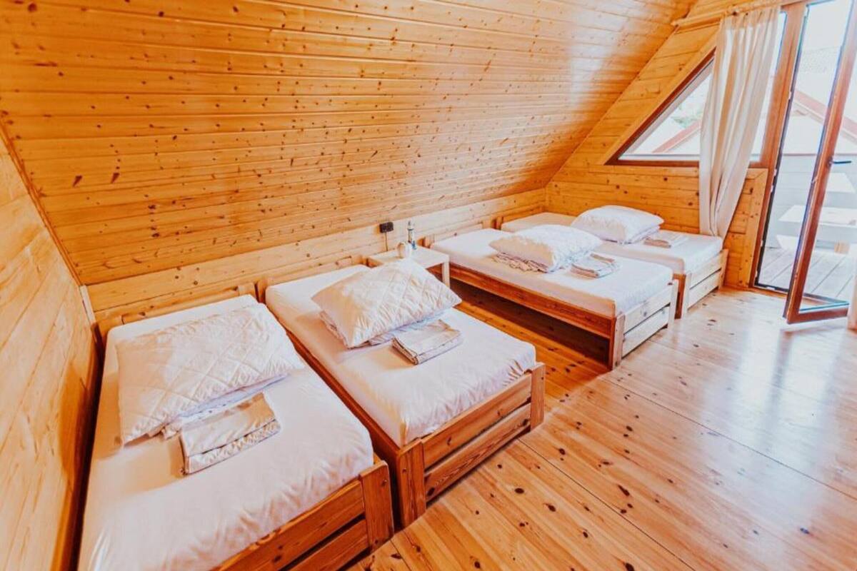 Eine Holzhütte mit vier Einzelbetten, die in einer Reihe angeordnet sind, jeweils mit Kissen und Decke.