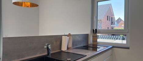 A modern kitchen with a black sink, white cabinets, and pendant lighting.