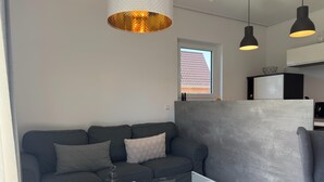 Ett modernt vardagsrum med en grå soffa, ett soffbord i glas och hängande lampor.