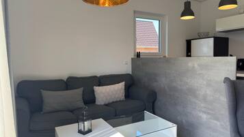 A modern living room with a grey sofa, a glass coffee table, and pendant lights.