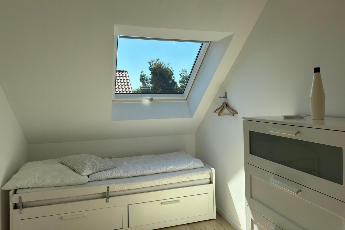 Een slaapkamer met dakraam, een bed, een dressoir en een flesje op het dressoir.
