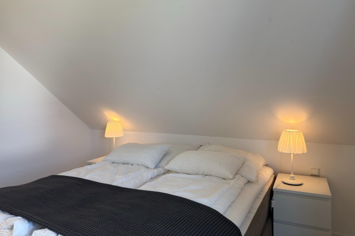 Un dormitorio con una cama, dos lámparas de noche, una mesita de noche y una manta negra.