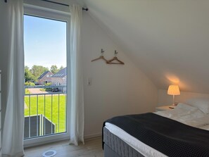 Un dormitorio con cama, una lámpara colgante, ventana con cortinas y vista a una casa y jardín.