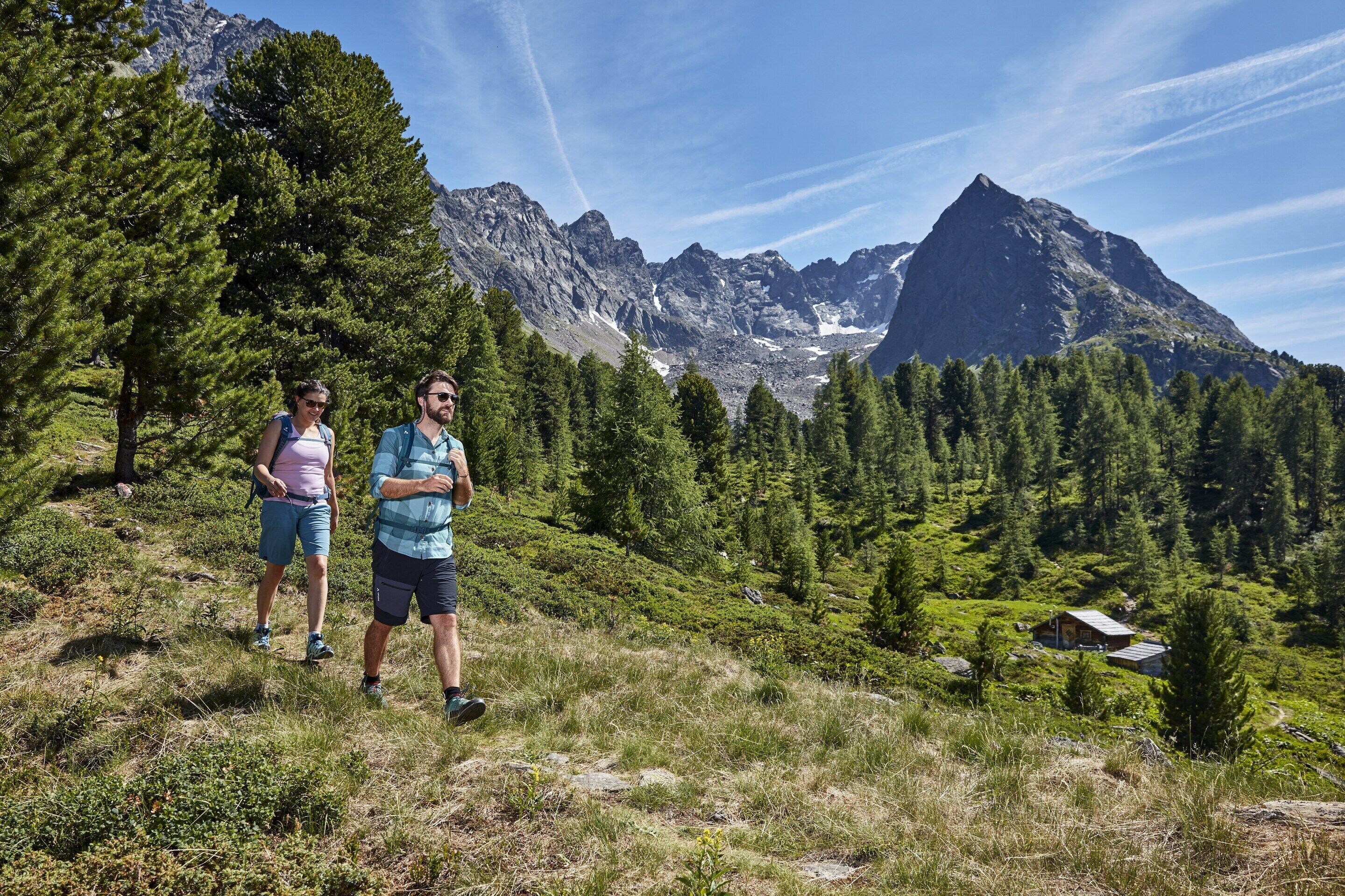 Two people standing on a grassy hill with a mountain range in the background.