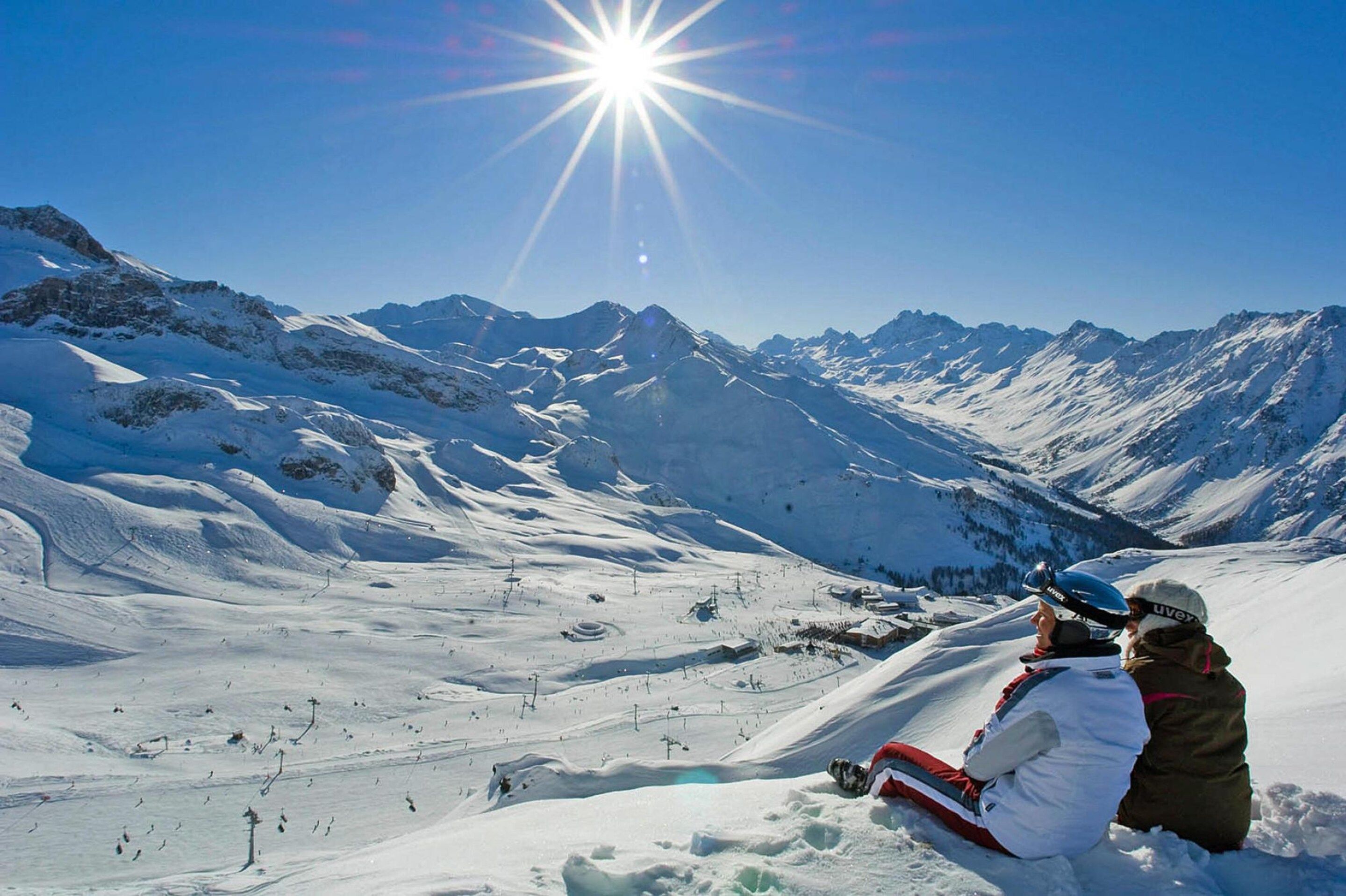 A snowy mountain landscape with a clear sky and a bright sun.