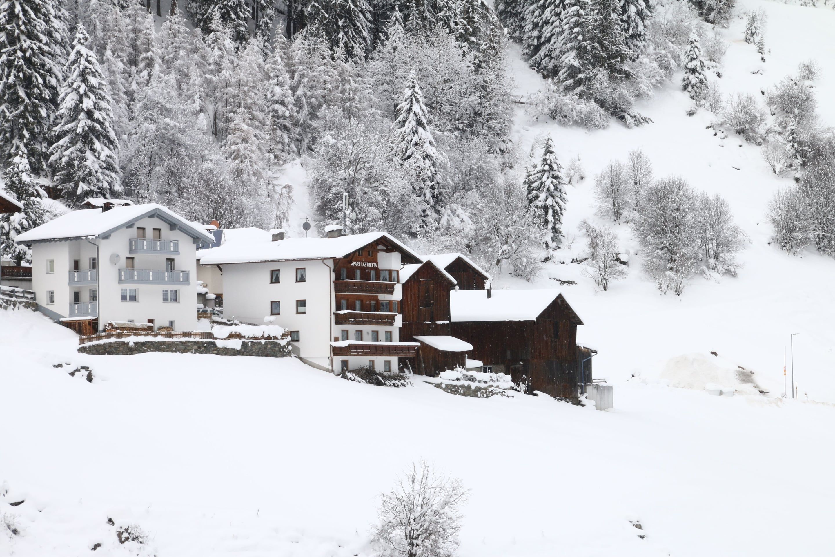 Un village de montagne enneigé, avec des bâtiments à plusieurs étages, dont un hôtel doté de balcons et un chalet en bois.