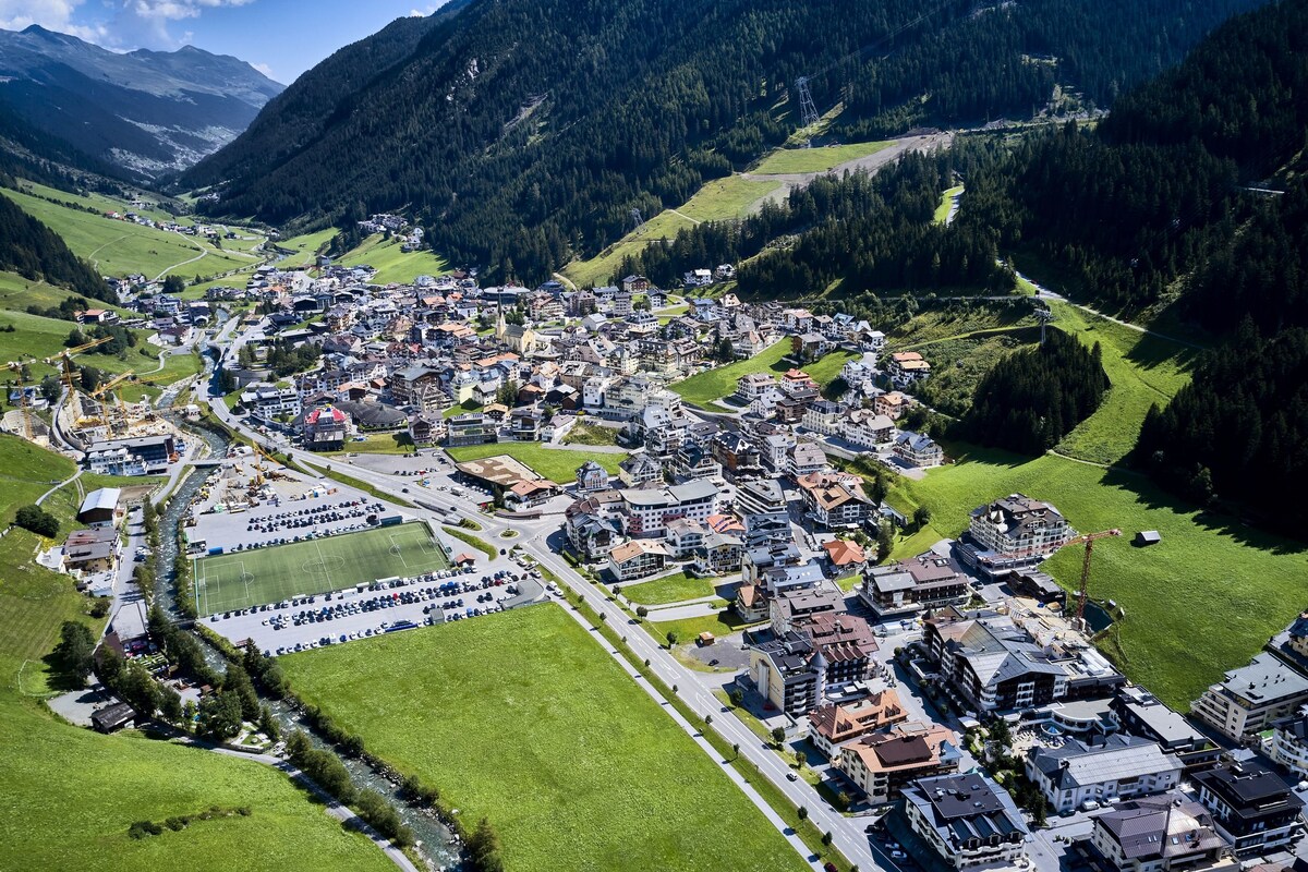 An aerial view of a town with a central road, buildings, and green spaces.