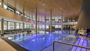 An indoor swimming pool with a wooden ceiling, glass walls, and a seating area with chairs. - Apartment in Ischgl Near Ski Lift (Ischgl)