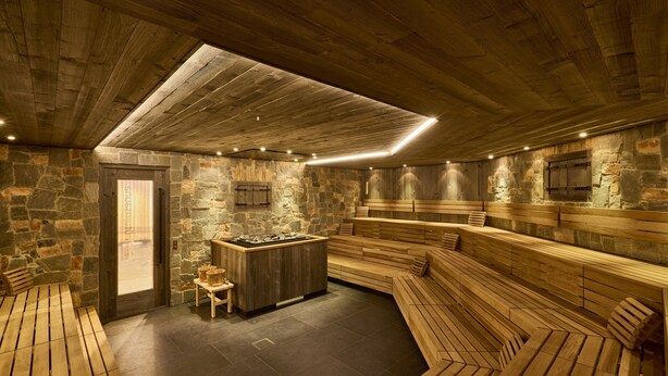 A sauna room with stone walls, wooden benches, and a central heated stone feature. - Apartment in Ischgl Near Ski Lift (Ischgl)