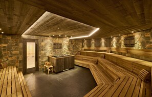 A sauna room with stone walls, wooden benches, and a central heated stone feature. - Apartment in Ischgl Near Ski Lift (Ischgl)