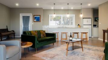 A modern living room with a sofa, a coffee table, and a dining area with stools.