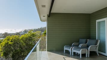 A balcony with two wicker chairs, a view of trees and distant mountains, and a green exterior wall.