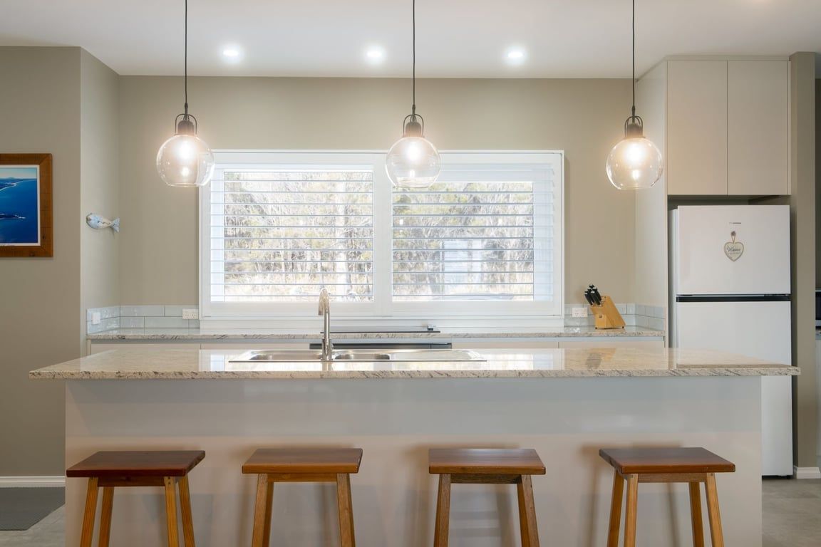 A kitchen with a central island, bar stools, pendant lights, a refrigerator, and a window with blinds.