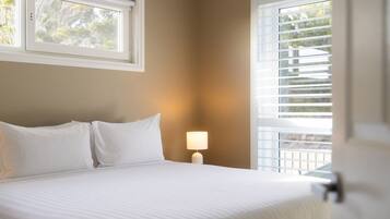 A hotel room with a bed, a nightstand with a lamp, and a window with blinds.
