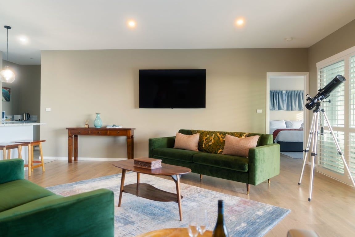 A living room with a green sofa, a coffee table, a flat-screen TV, and a telescope.