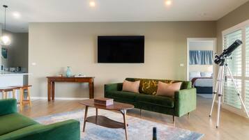 A living room with a green sofa, a coffee table, a flat-screen TV, and a telescope.