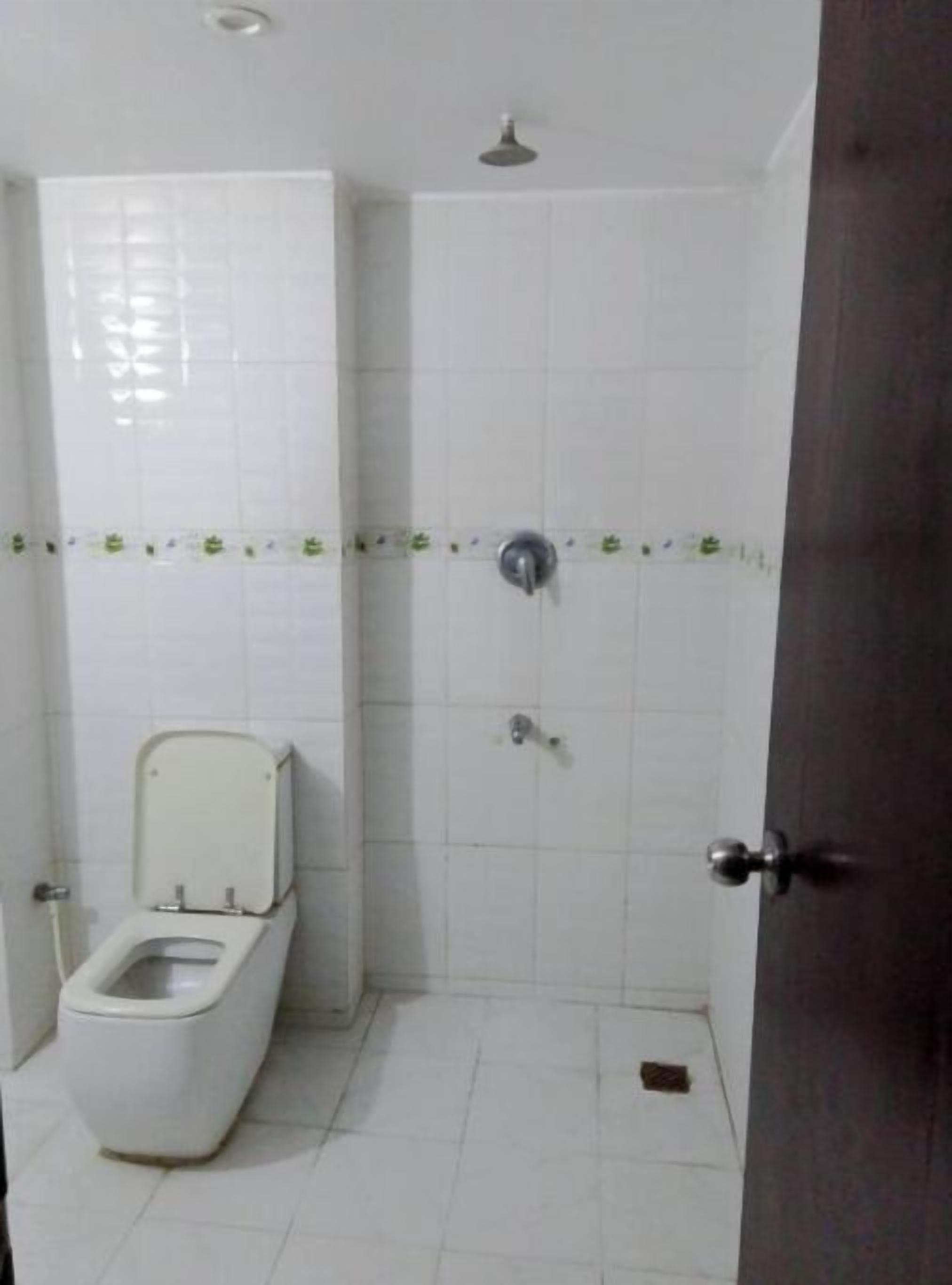A small, tiled bathroom with a toilet, a shower, and a door.