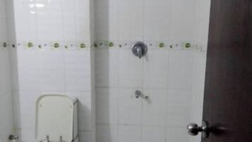 A small, tiled bathroom with a toilet, a shower, and a door.