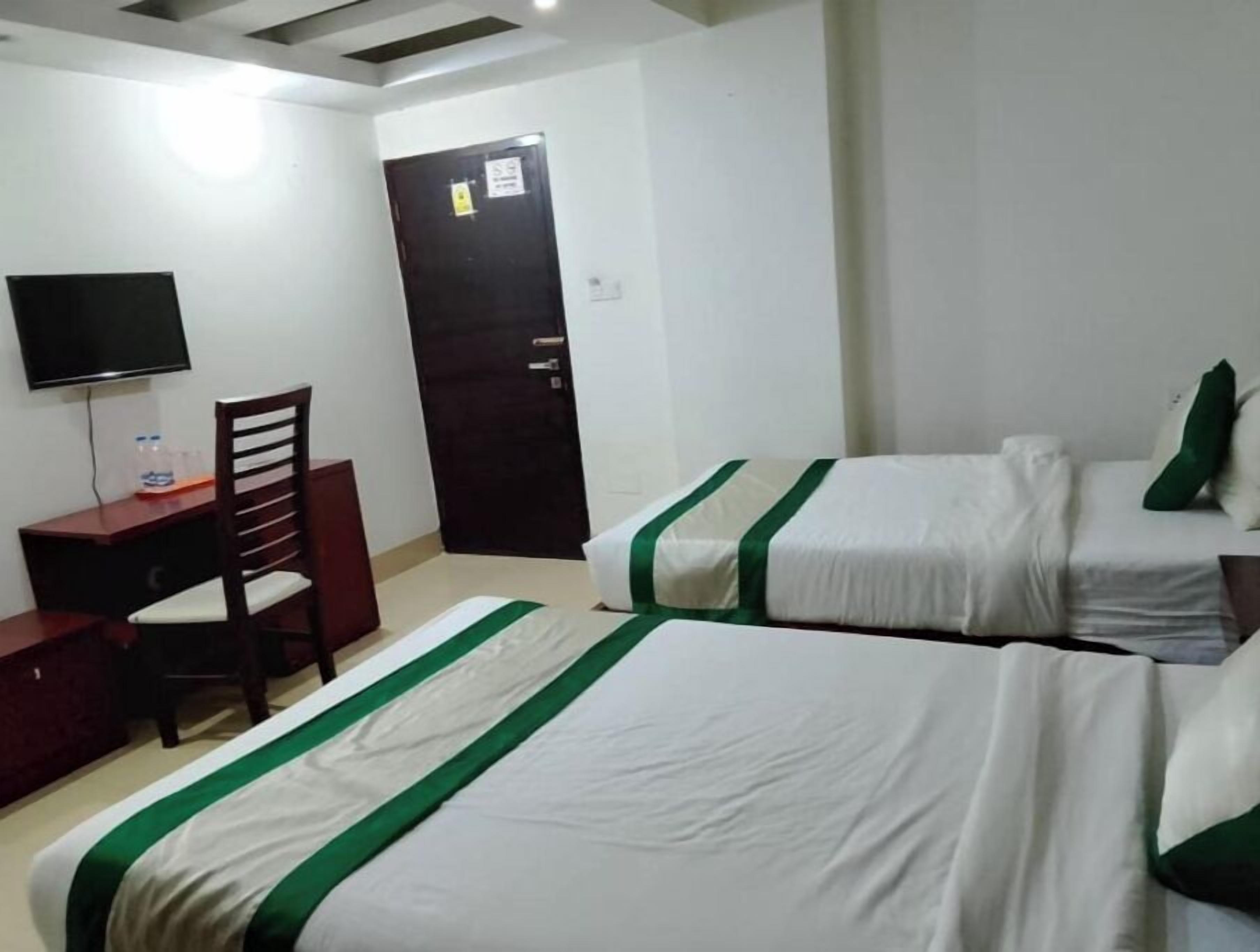 Una habitació d'hotel amb dos llits, un escriptori, una cadira, un televisor i una porta.