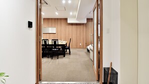 Um corredor leva a uma sala de jantar com uma mesa, cadeiras, um sofá e uma cesta de armazenamento preta.