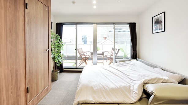 Quarto com cama, guarda-roupa, porta de vidro deslizante para uma varanda e uma planta em vaso.