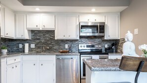 A modern kitchen with white cabinets, a stainless steel dishwasher, a built-in oven, and a granite countertop. - 3BR The Montrose Collective C! Steps to Food & Fun! (Houston)