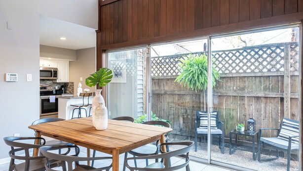 A dining area with a wooden table and chairs, a vase with a plant, and a view of a backyard through large sliding glass doors. - 3BR The Montrose Collective C! Steps to Food & Fun! (Houston)