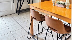 A dining area with a wooden table, two chairs, a small side table with a pink box, and a microwave in the background.