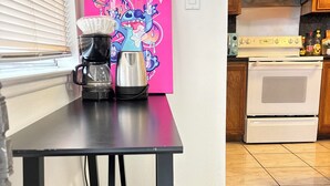 A kitchen with a coffee maker, a kettle, and a pink painting on the wall.