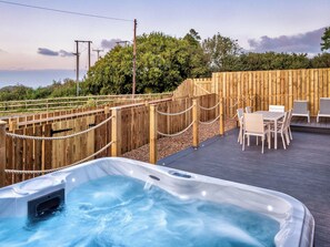 Ein Whirlpool auf einer Holzterrasse mit Blick auf Bäume und einen Holzzaun.