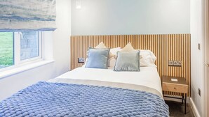 Ett sovrum med en säng, ett sängbord, ett litet bord, ett fönster och en hängande lampa.