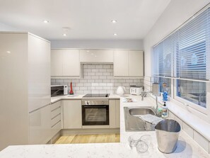 Una cocina moderna con armarios blancos, horno integrado, microondas, hervidor y lavaplatos.