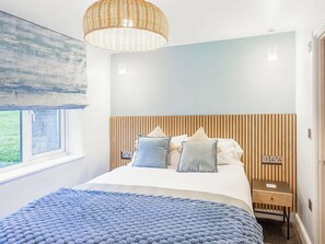 A bedroom with a bed, a bedside table, a nightstand, a window, and a hanging light fixture.