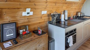 A kitchen with wooden walls, a skylight, a sink, a stove, and a trash bin. - The Rounton - UKC9284 (Brompton)