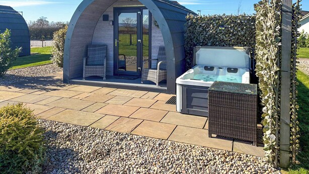 A small outdoor hot tub area with a covered seating space, a hot tub, and a sign reading 'Valley Pods.' - The Rounton - UKC9284 (Brompton)