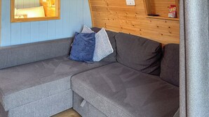 A grey sectional sofa with a wooden floor, a blue wall with a window, and a wooden wall with a shelf. - The Rounton - UKC9284 (Brompton)
