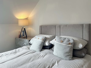 A neatly made bed with striped bedding, a grey upholstered headboard, and two bedside tables with lamps and decorative items. - 4 bedroom accommodation in Peebles (Peebles)
