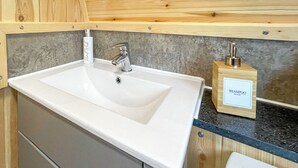 A bathroom with a white sink, wooden cabinets, and a wooden shampoo dispenser on the countertop. - The Welbury - UKC9285 (Brompton)