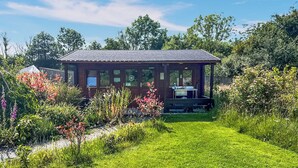 Une cabane en bois dotée d’un porche, entourée d’un jardin bien entretenu et d’arbres.