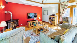 A living room with a red wall, a TV, a fireplace, a bookshelf, and a large window with curtains. - Heads Nook Hall Cottage (Brampton)