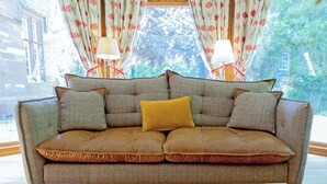 A sofa with cushions, a table with magazines and a book, and a window with curtains. - Heads Nook Hall Cottage (Brampton)