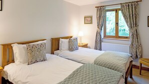 A double bed with a quilted green blanket, a wooden headboard, and a bedside table with a lamp. - Heads Nook Hall Cottage (Brampton)