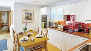 A modern kitchen with white cabinets, a wooden dining table, and a red tiled backsplash. - Heads Nook Hall Cottage (Brampton)