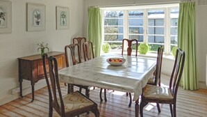 Ein Esszimmer mit Tisch, Stühlen, einer Chandelieber und Blick durch große Fenster.