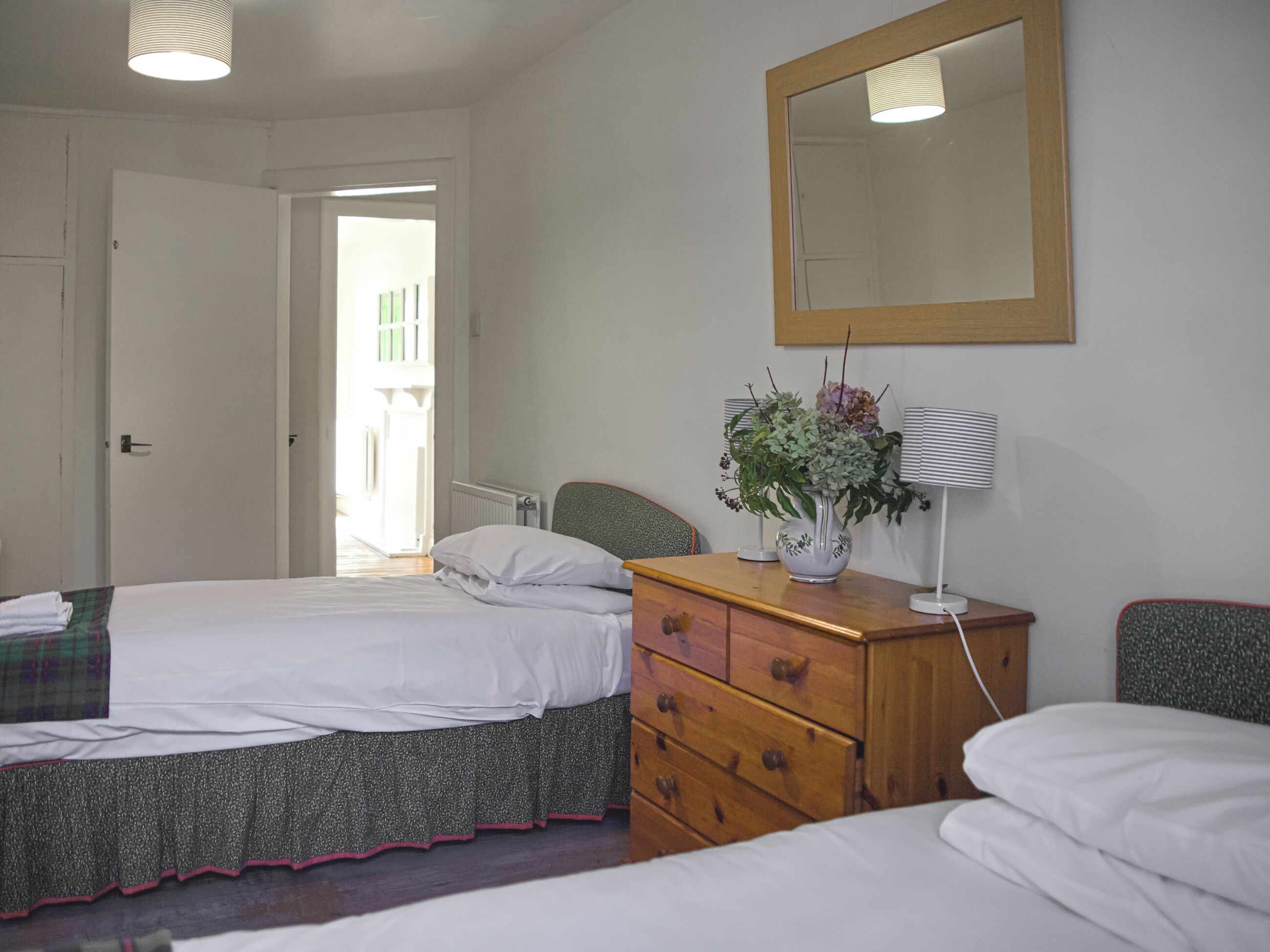 A bedroom with two beds, a dresser, a mirror, and a window.