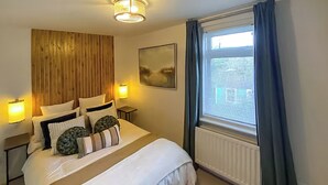 A bedroom with a large bed, bedside lamps, a wooden headboard, a window with curtains, and a radiator. - 2 bedroom accommodation in Newcastle Upon Tyne (Newcastle Upon Tyne)