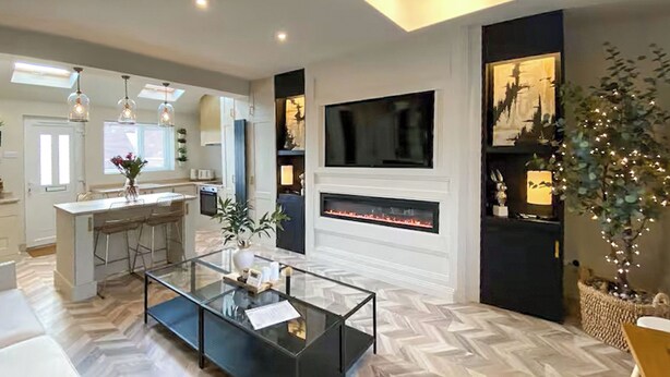 A modern living room with a glass coffee table, a fireplace, a TV mounted on the wall, and a kitchen area visible through an open door. - 2 bedroom accommodation in Newcastle Upon Tyne (Newcastle Upon Tyne)